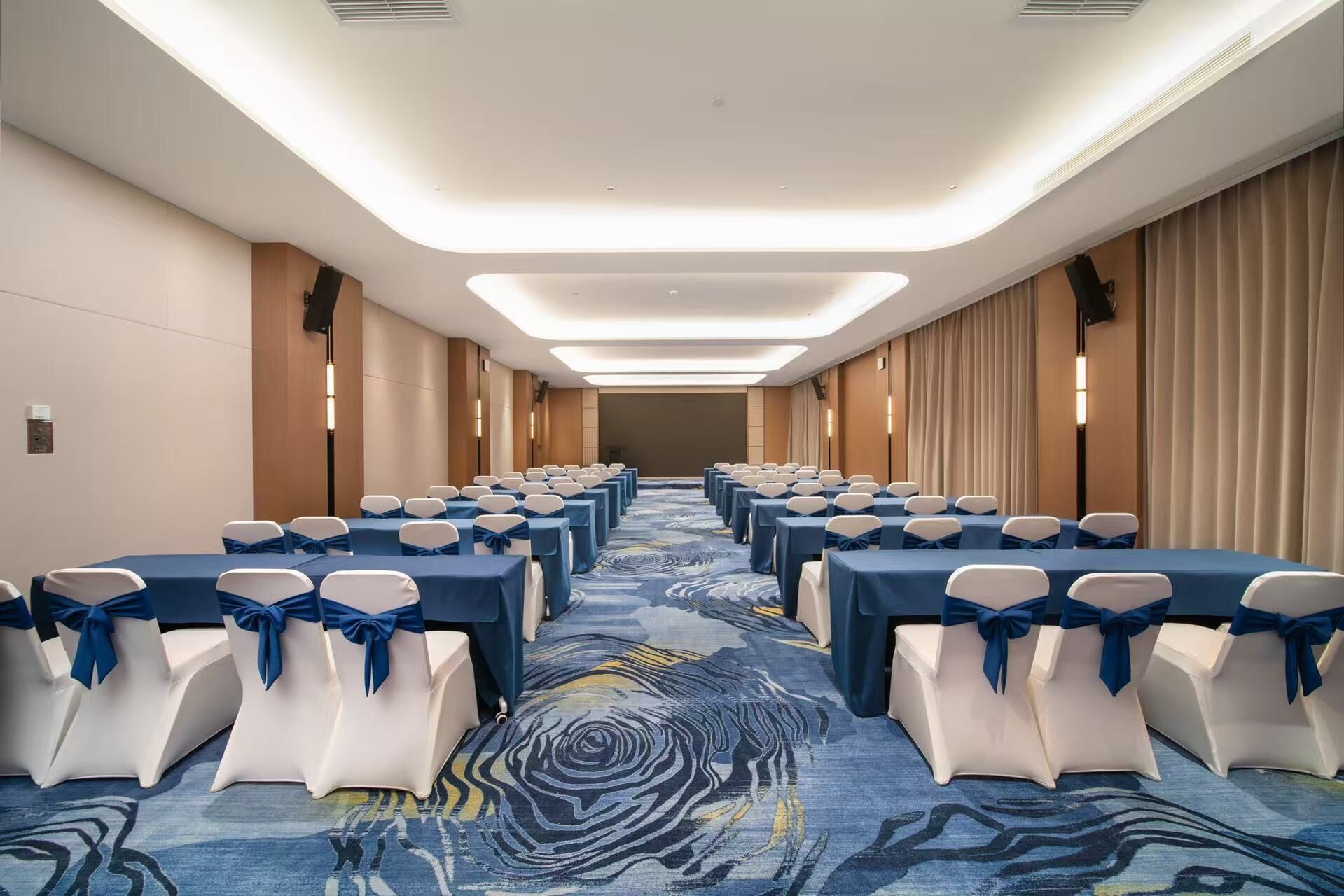 Un salón de conferencias de hotel con filas de mesas, sillas y una alfombra estampada.