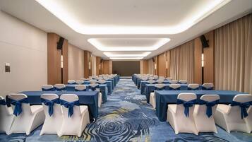 Un salón de conferencias de hotel con filas de mesas, sillas y una alfombra estampada.