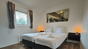 A hotel room with a bed, two bedside tables, a window with curtains, a wall-mounted painting, and a radiator. - Holiday Home in Kaatsheuvel With Terrace (Kaatsheuvel)