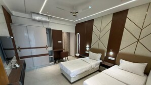 Quarto de hotel com duas camas, uma escrivaninha, uma cadeira, uma televisão e um ventilador de teto.