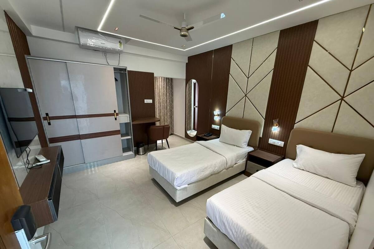 Une chambre d’hôtel avec deux lits, un bureau, une chaise, une télévision et un ventilateur de plafond.
