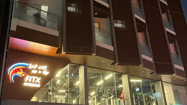 Edifício de vários andares com academia e centro de fitness no térreo, com grandes janelas e sacadas.
