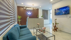 Een moderne hotel receptie met een blauwe bank, een glazen salontafel, een receptiebalie en een aan de muur bevestigde televisie.