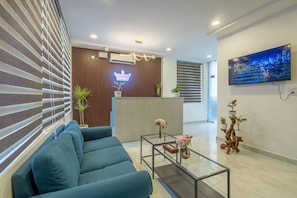 A modern hotel reception area with a blue sofa, a glass coffee table, a reception desk, and a TV mounted on the wall. - RCC Hotels Helix Gachibowli (Hyderabad)
