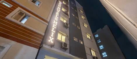 A multi-story hotel with illuminated signage, air conditioning units, and a modern architectural design.