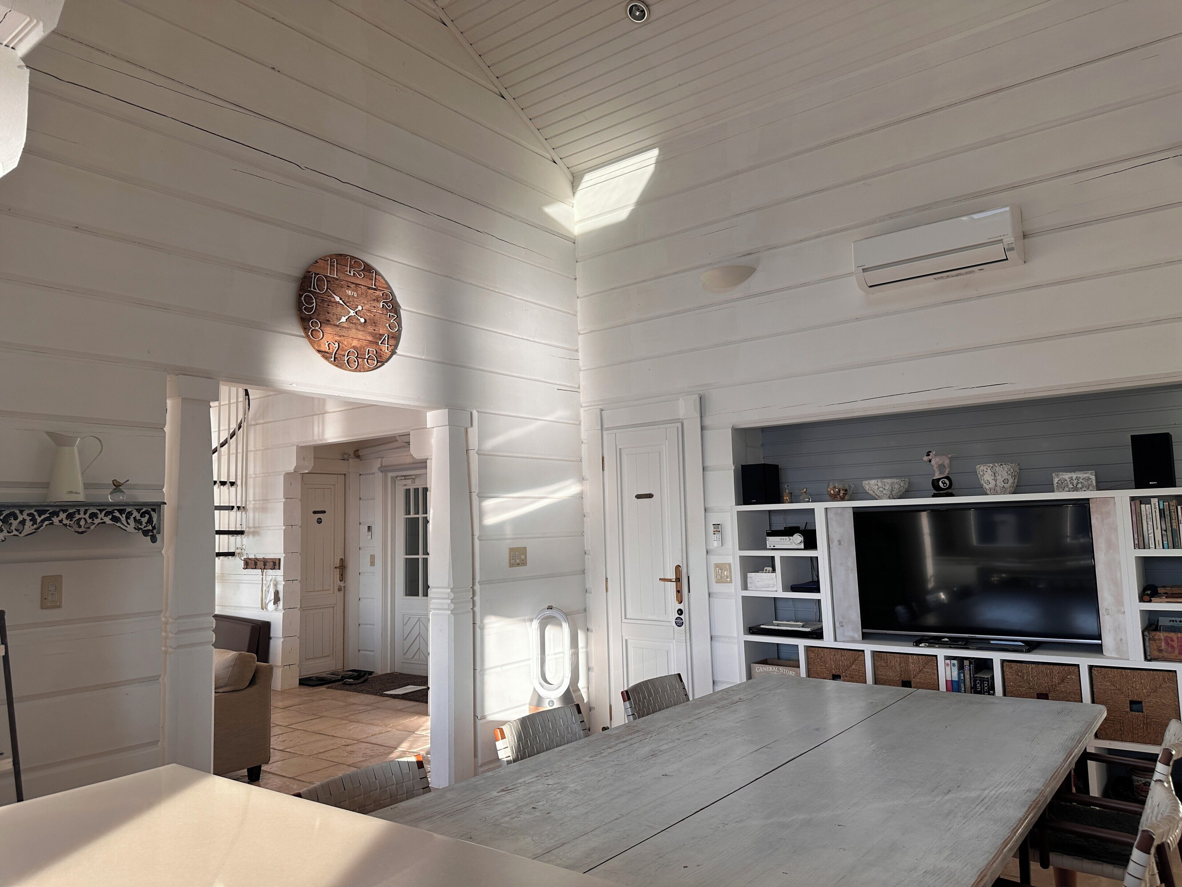 Une cuisine spacieuse avec une grande table à manger, des murs en bois peints en blanc et un téléviseur encastré.