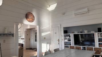 Une cuisine spacieuse avec une grande table à manger, des murs en bois peints en blanc et un téléviseur encastré.