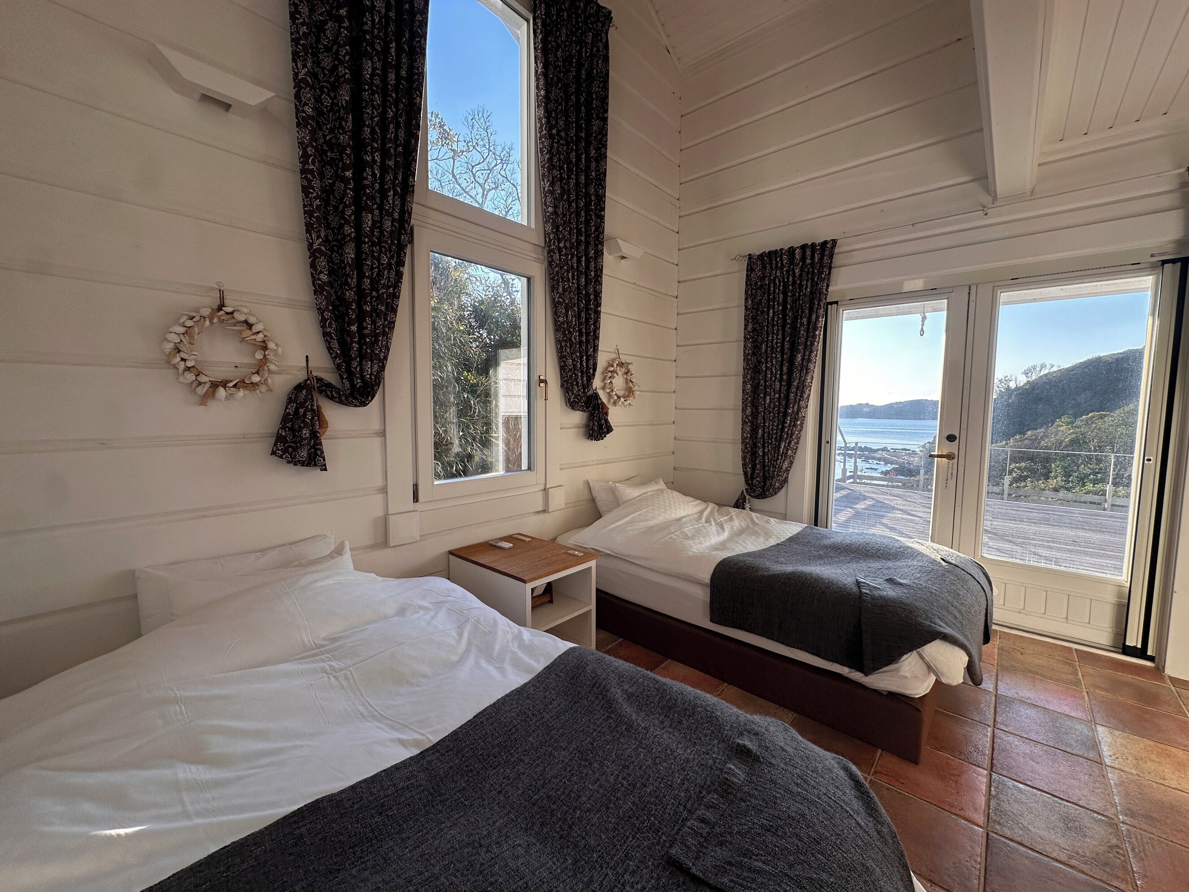 Una habitación con dos camas, una mesita y vista al mar por una puerta.