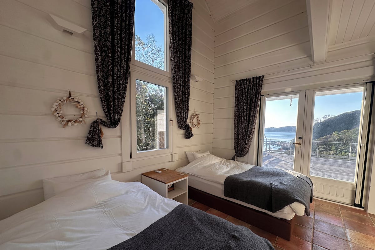 A room with two beds, a small table, and a view of the sea.