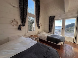 A room with two beds, a small table, and a view of the sea. - Casa Della Nonna (Kawazu)