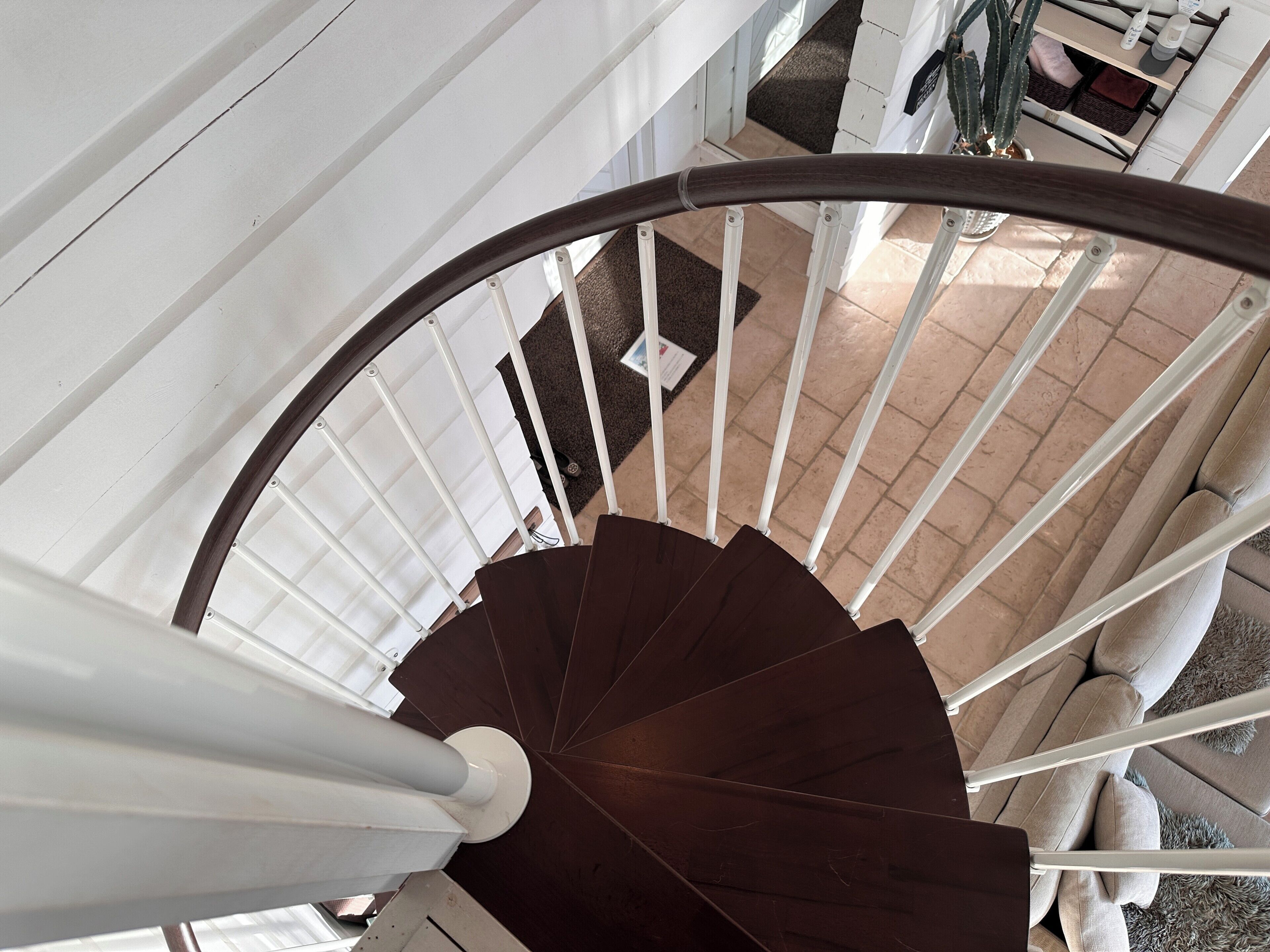 A spiral staircase with white railings and dark steps, leading to a landing area with a door and a small plant.