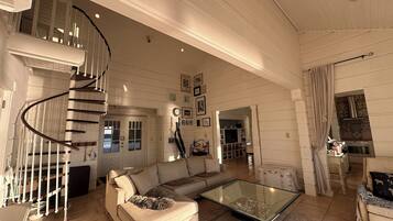 Un salon spacieux avec un escalier en colimaçon, une table basse en verre et un canapé beige.