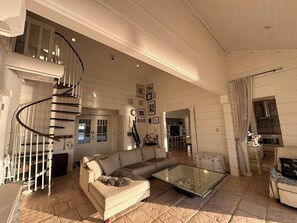 Un salón espacioso con una escalera en espiral, una mesa de centro de cristal y un sofá color beige.