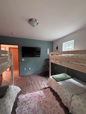 Ein Zimmer mit Stockbetten, einem an der Wand befestigten Fernseher und einem Fenster.
