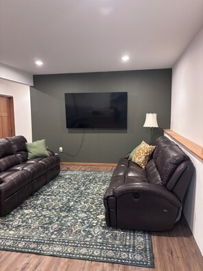 Ein Wohnzimmer mit zwei Ledersofas, einem gemusterten Teppich, einem Flachbildfernseher und einer Lampe.