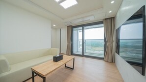 A modern room with a sofa, a wooden table, and large windows offering a view of the sea.