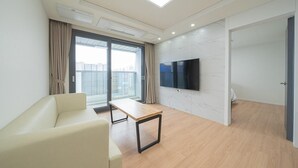 Una sala de estar moderna con un sofá, una mesa de madera, un televisor de pantalla plana montado en la pared y un amplio ventanal con cortinas.