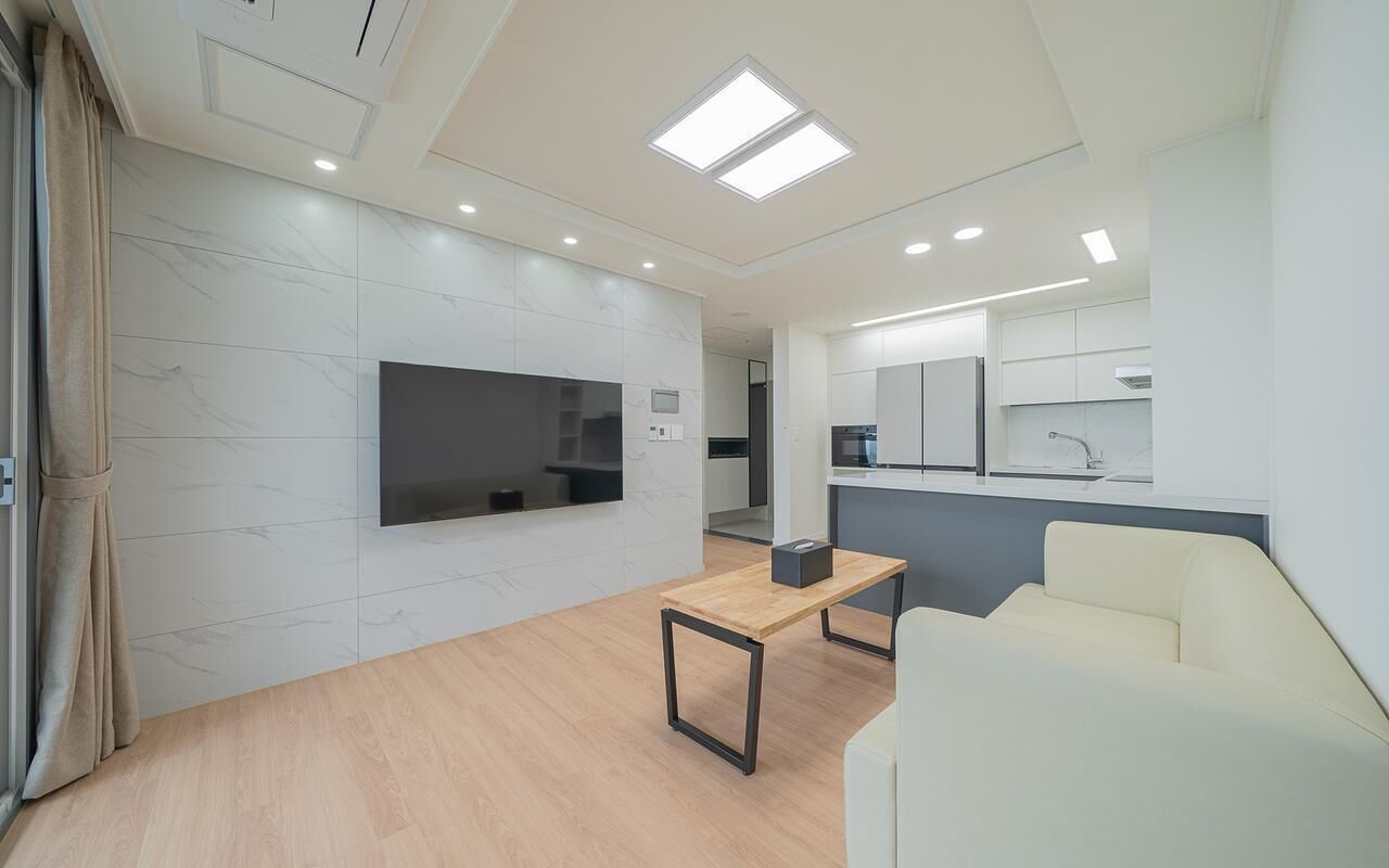 A modern living room with a flat-screen TV, a wooden coffee table, a sofa, and a kitchen area in the background.