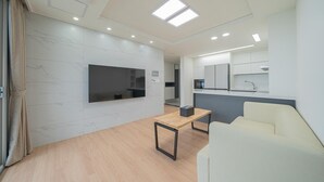 Una sala de estar moderna con un televisor de pantalla plana, una mesa de centro de madera, un sofá y una cocina al fondo.