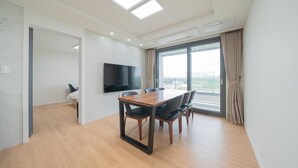 Una habitación de hotel moderna con un ventanal grande, un televisor de pantalla plana, una mesa de comedor de madera y un sofá.
