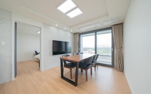 Una habitación de hotel moderna con un ventanal grande, un televisor de pantalla plana, una mesa de comedor de madera y un sofá.