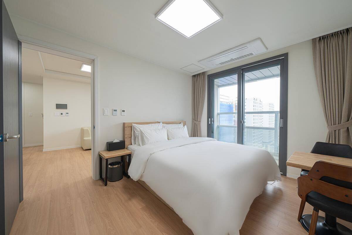 Hotellihuone, jossa on sänky, yöpöytä, tuoli ja ikkuna, jossa on verhot.