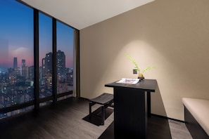 Una habitación de hotel moderna con un gran ventanal que ofrece vistas a la ciudad, un pequeño escritorio con una planta y un banco.