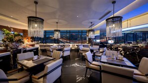 Un restaurante moderno con techos altos, candelabros colgantes y vistas a la ciudad.