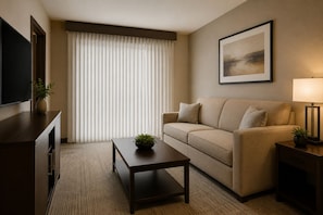 Ein Hotelzimmer mit einer Couch, einem Couchtisch, einem Fernseher, einer Lampe und einem Bild an der Wand.