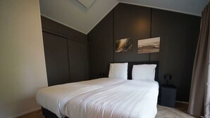 Un dormitorio moderno con una cama grande, paredes oscuras y dos obras de arte colgadas en la pared.