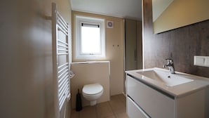 Un baño pequeño con inodoro, ventana, radiador, lavabo y espejo.