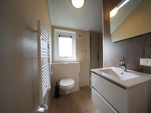 Ein kleines Badezimmer mit Toilette, Fenster, Heizkörper, Waschbecken und Spiegel.