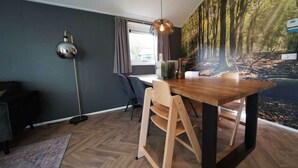 Un comedor moderno con una mesa de madera, sillas, una lámpara colgante y un mural temático de bosque.