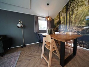 Ein moderner Essbereich mit Holztisch, Stühlen, einer Pendelleuchte und einer Wandmalerei zum Thema Wald.