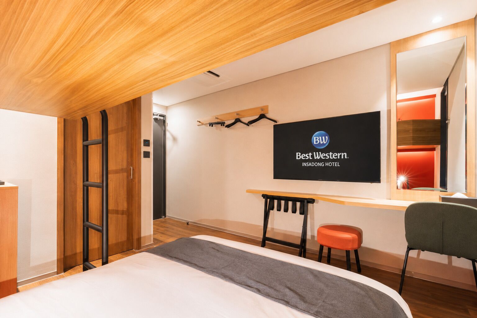 A hotel room with a bed, a desk, a chair, a TV, and a mirror.