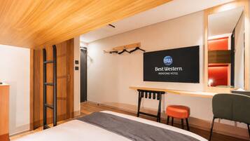 A hotel room with a bed, a desk, a chair, a TV, and a mirror.