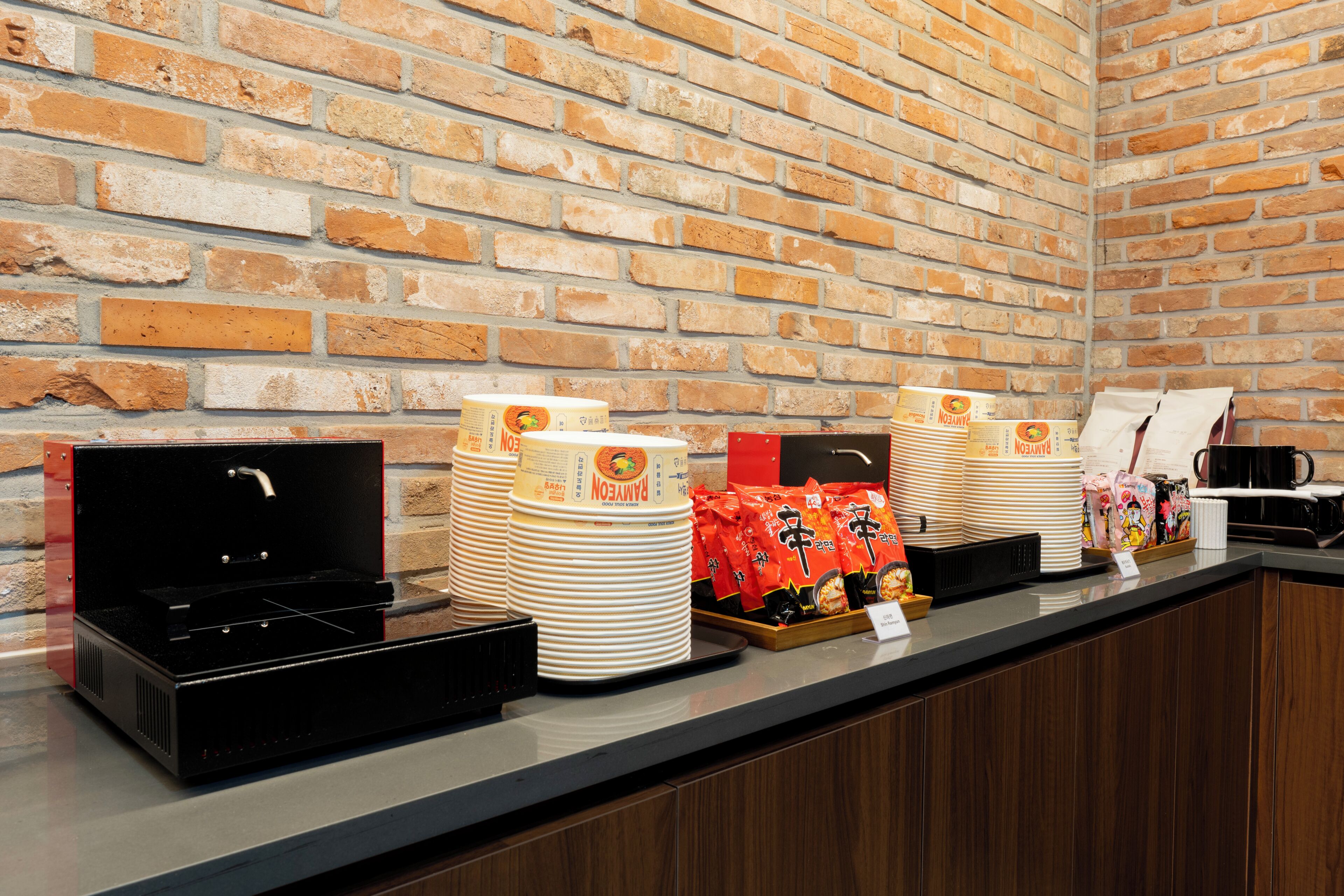 A buffet setup with stacked plates, a microwave, and a tray of snacks against a brick wall.