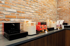 A buffet setup with stacked plates, a microwave, and a tray of snacks against a brick wall. - Best Western Insadong Hotel (Seoul)