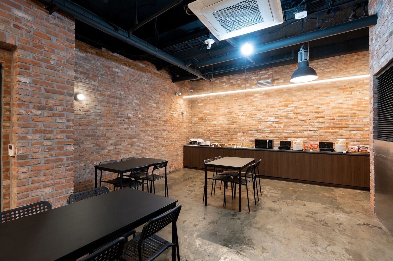A brick-walled room with a bar area, tables, and chairs.