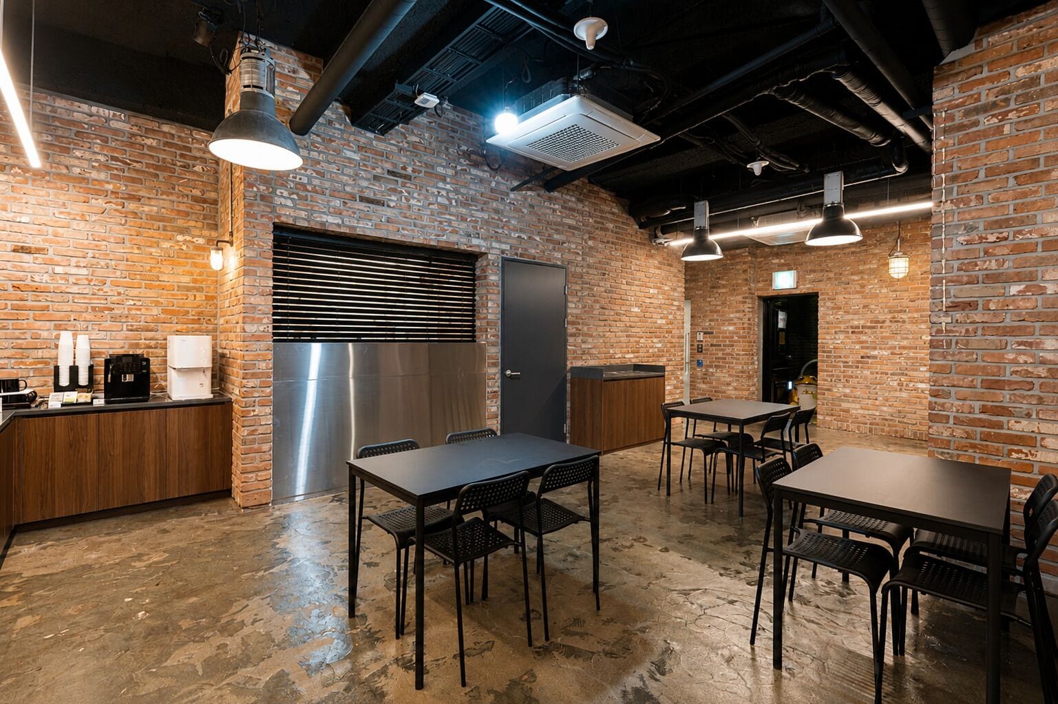 A modern kitchen with brick walls, stainless steel appliances, and a seating area with tables and chairs.