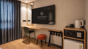 Ein Hotelzimmer mit Flachbildfernseher an der Wand, einem Holztisch, einem roten Sessel, einer kleinen Küchenzeile mit Mikrowelle und einer Kaffeemaschine.