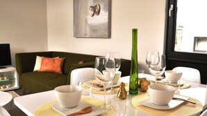 A dining table set with white bowls, glasses, and a green bottle, with a green couch and a painting in the background. - Holiday Home in Breskens With Terrace (Breskens)