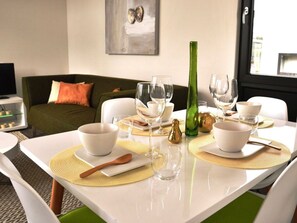 Ein Esstisch ist gedeckt mit weißen Schüsseln, Gläsern und einer grünen Flasche, im Hintergrund ein grünes Sofa und ein Gemälde.