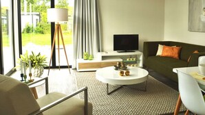 A modern living room with a sofa, coffee table, TV, and a large window with curtains. - Holiday Home in Breskens With Terrace (Breskens)