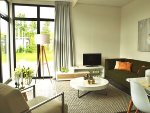 Ein modernes Wohnzimmer mit einer Couch, einem Couchtisch, einem Fernseher und einem großen Fenster mit Vorhängen.