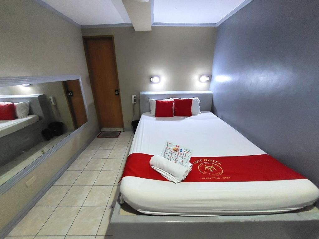 A hotel room with a bed, a mirror, a door, and a light fixture.