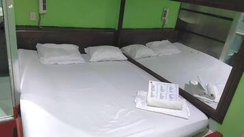 A double bed with white bedding, a mirror, and a wall-mounted phone.