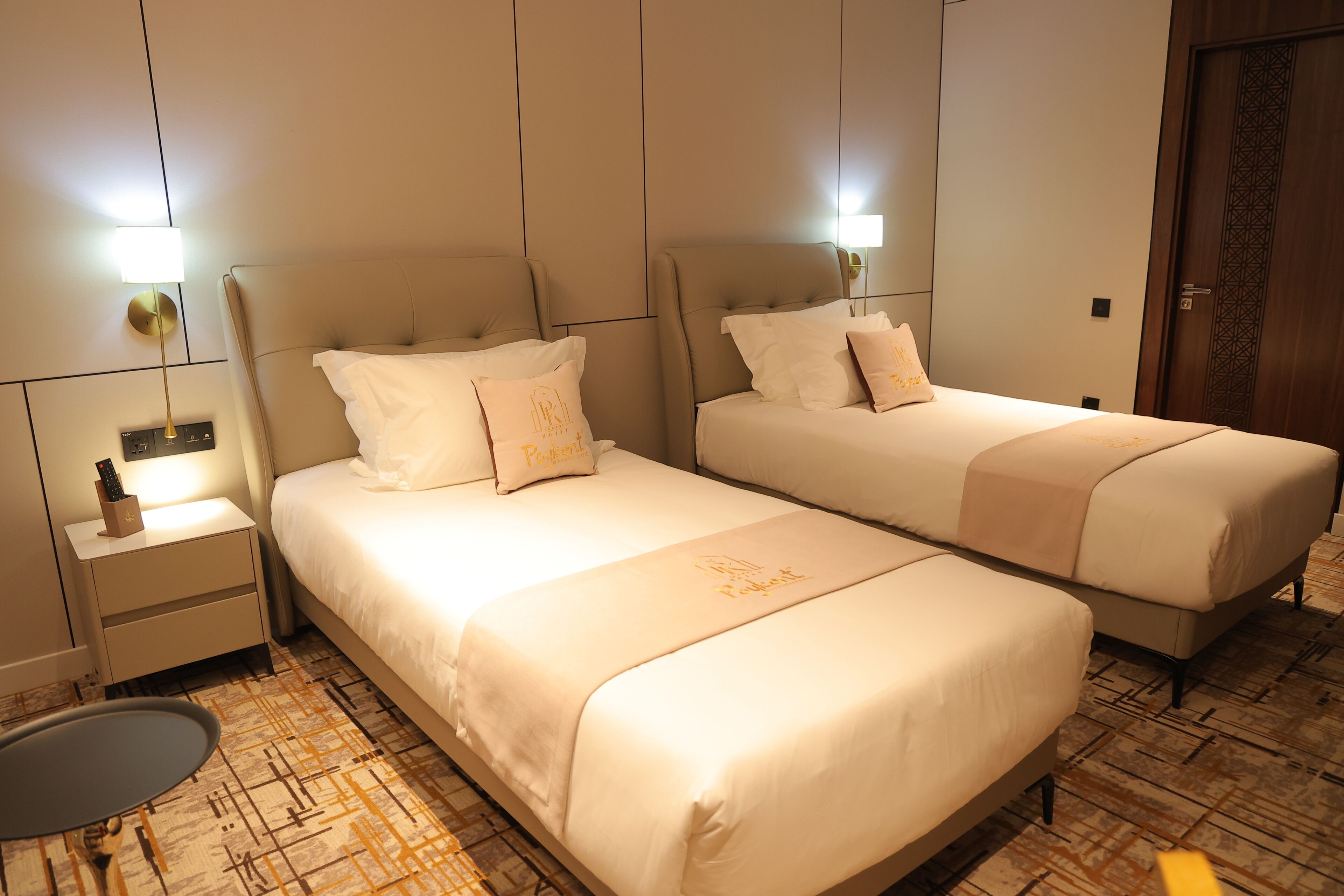 A hotel room with two beds, a bedside table, a lamp, and a patterned carpet.