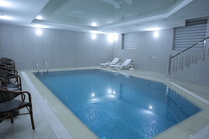An indoor swimming pool with clear water, surrounded by lounge chairs and a staircase.