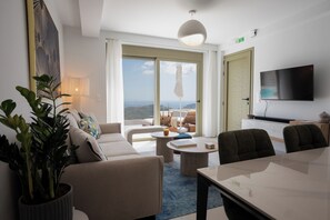 Ein Hotelzimmer mit einer Sitzecke, Stühlen, einem Esstisch, einem Fernseher und einem großen Fenster mit Blick.